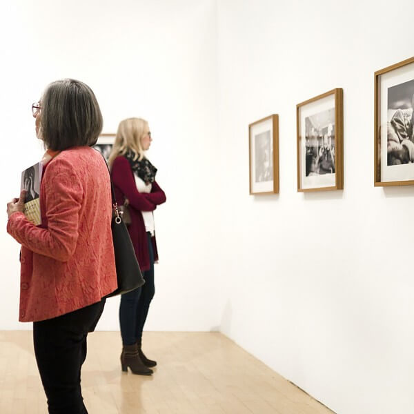 Zwei Frauen betrachten gerahmte schwarz-weiße Fotografien an einer weißen Museumswand