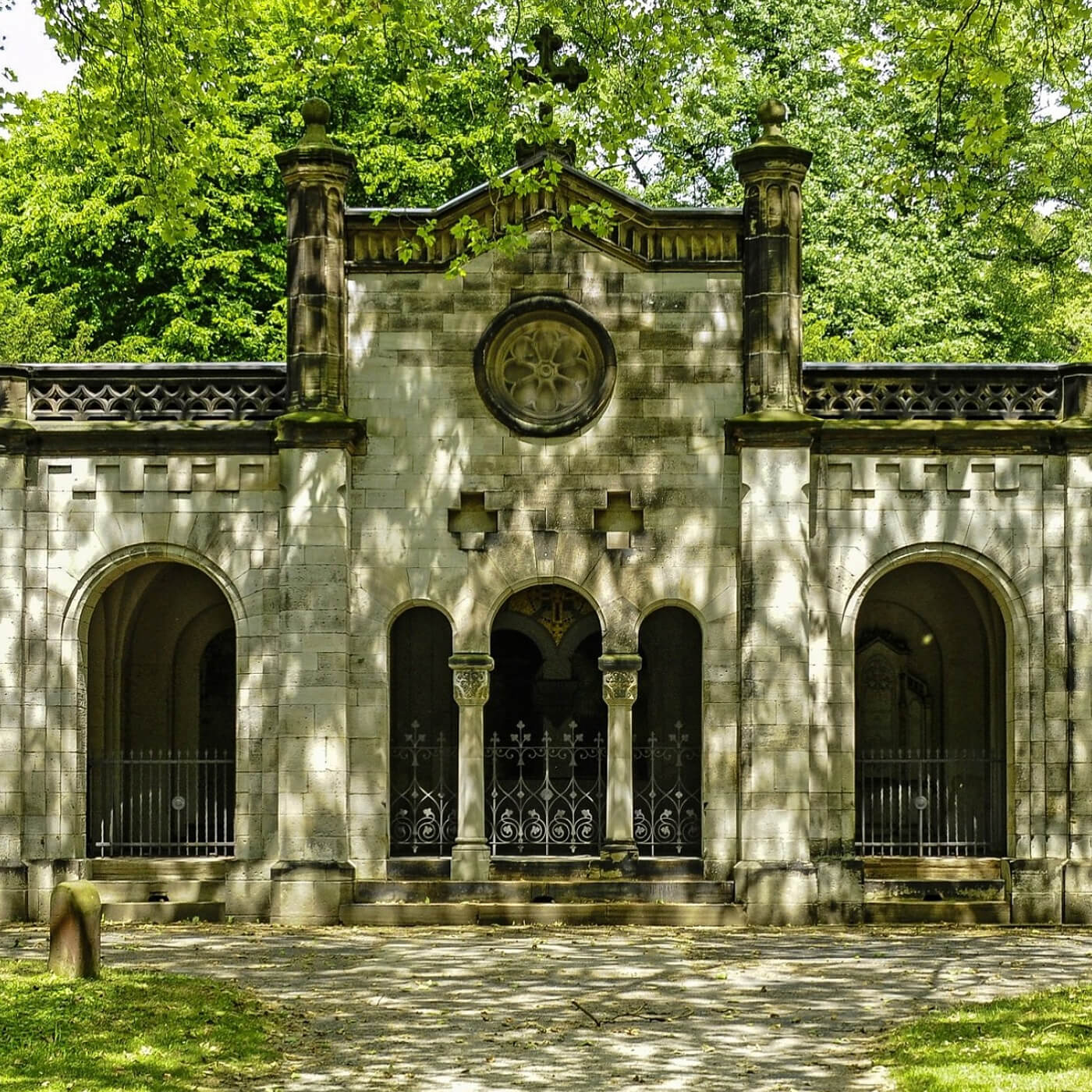 Fassade eines historischen Gebäudes mit Rundbögen, Säulen, umgeben von Bäumen