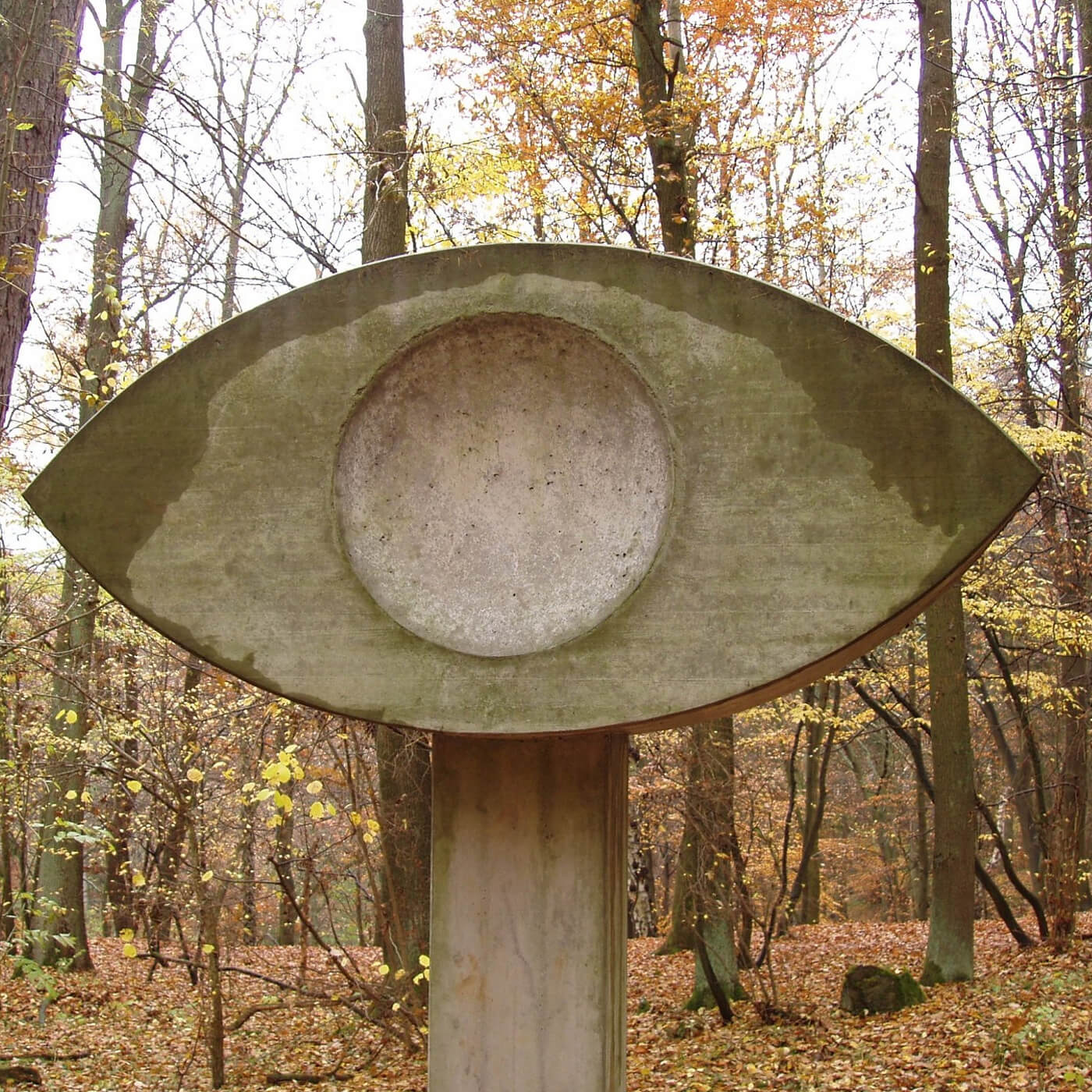 Große steinerne Skulptur in Form eines Auges in einem herbstlichen Wald