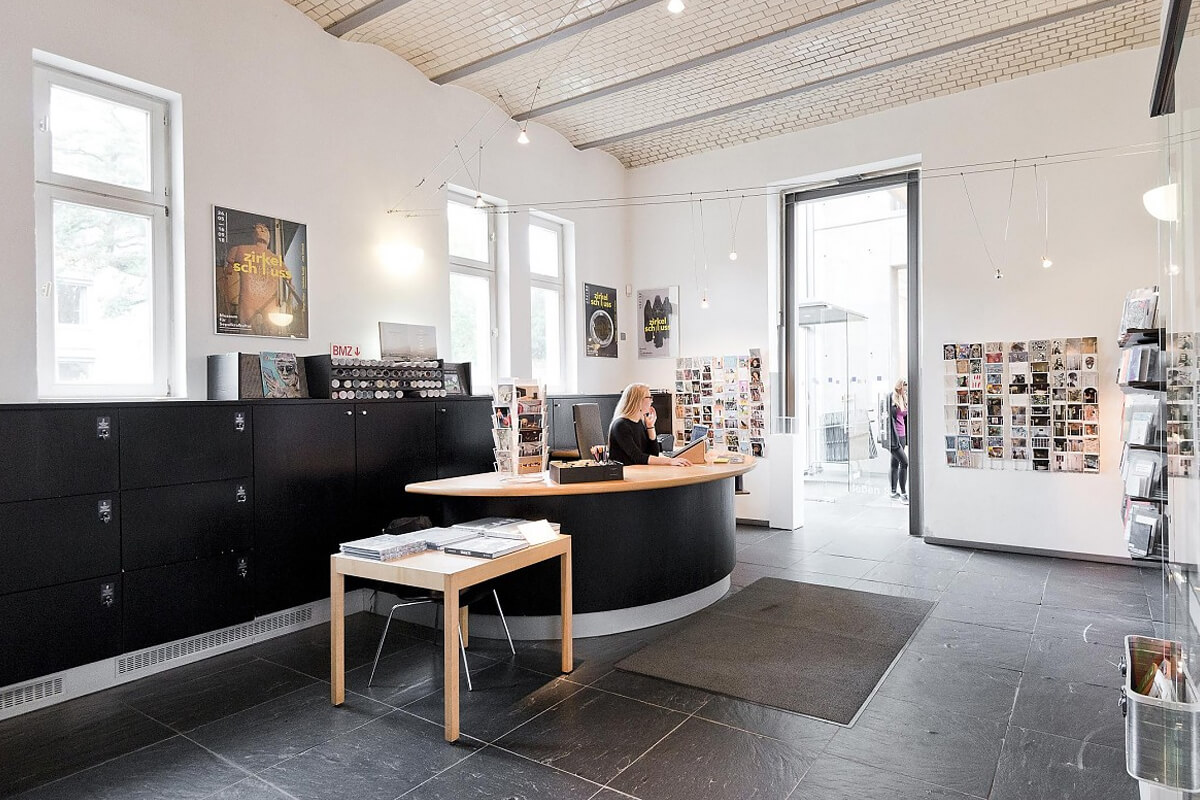 Bright museum reception desk with ticket seller behind the counter and black cabinets in the background.
