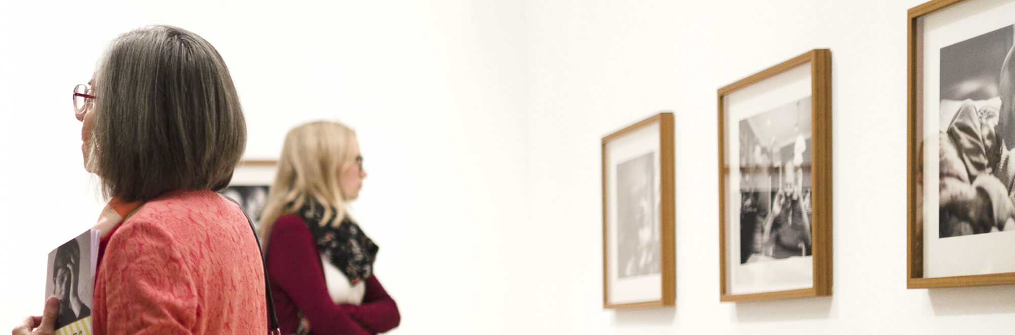 Zwei Frauen betrachten gerahmte schwarz-weiße Fotografien an einer weißen Museumswand