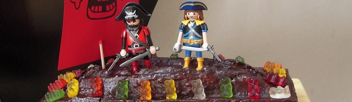 Schokoladentorte mit zwei Playmobil-Figuren in Piratenkostümen und einer Reihe bunter Gummibärchen am Rand