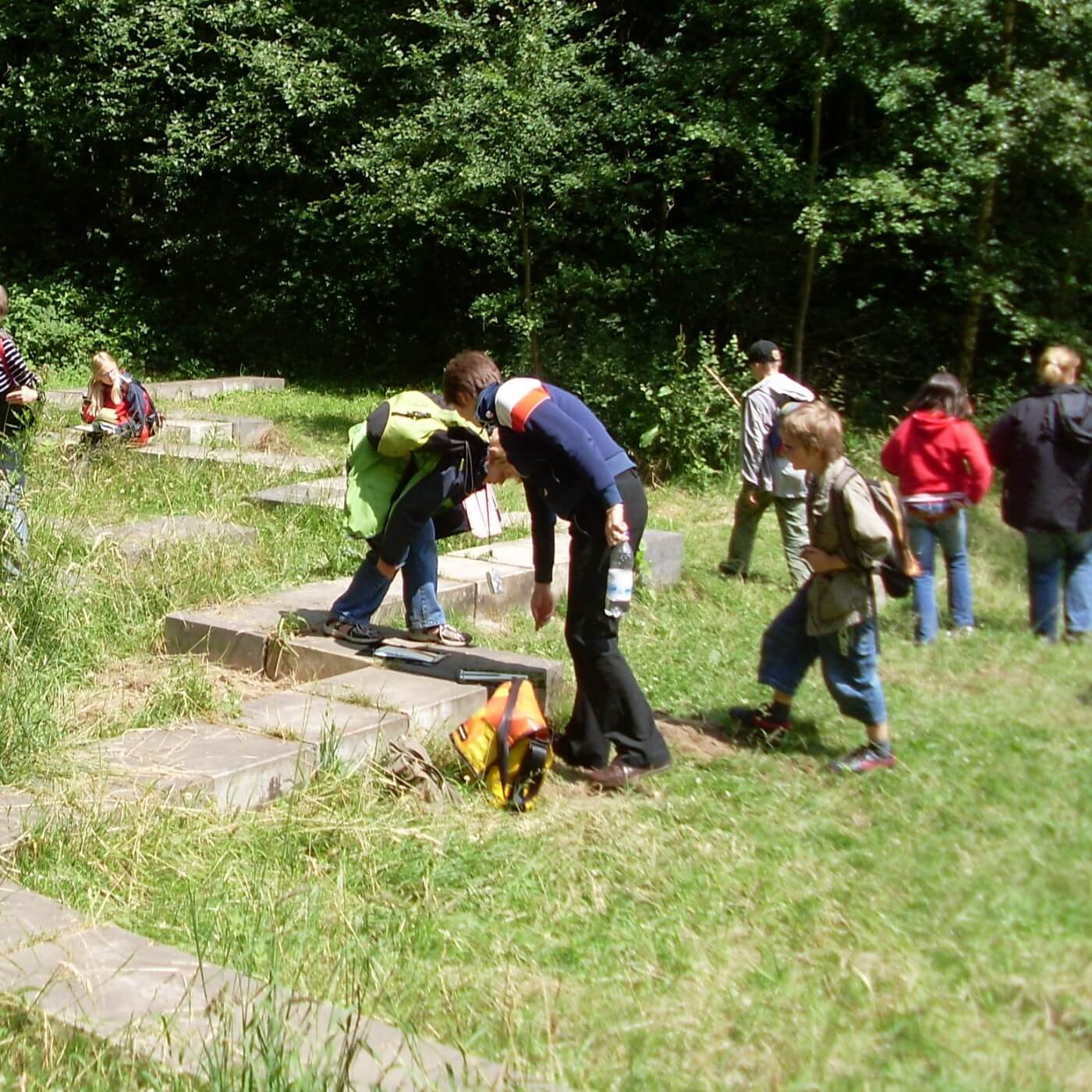 Gruppe von Kindern und einer erwachsenen Person auf einer Wiese mit Steinplatten