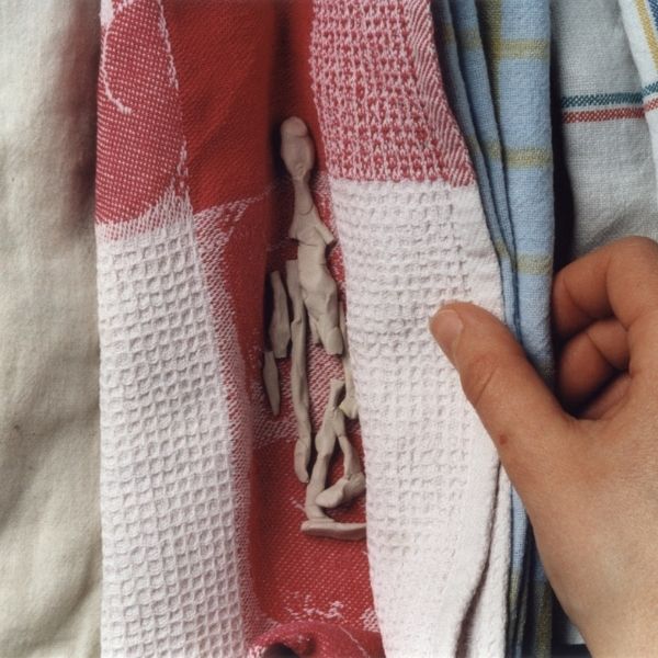 Eine Hand hebt eine Falte eines Tuchs an und enthüllt eine winzige Tonfigur.