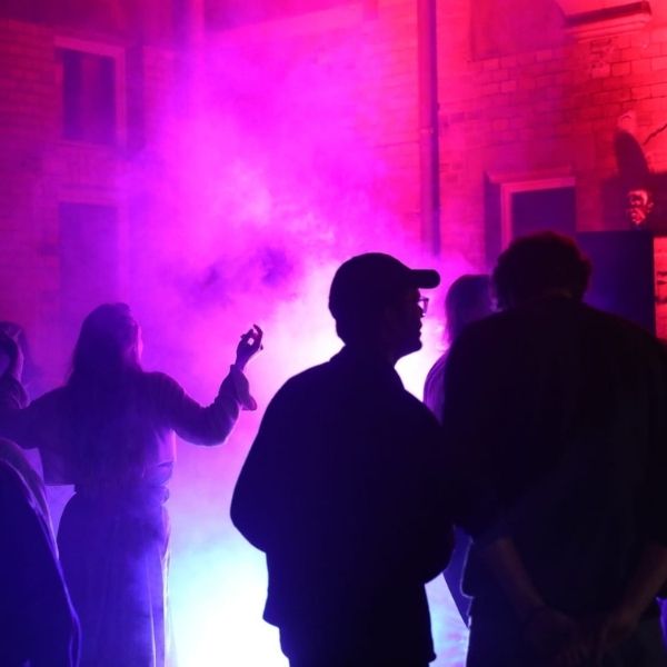 Tanzende Menschen im Innenhof des Museums für Sepulkralkultur, nachts. Buntes Licht, Nebel.